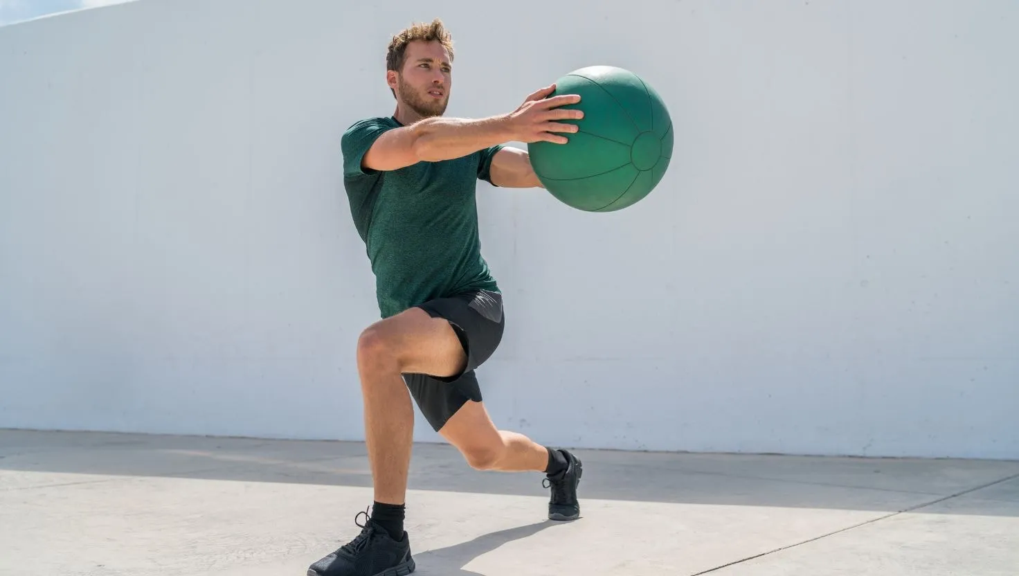 Man doing walking lunges outdoors while holding a medicine ball